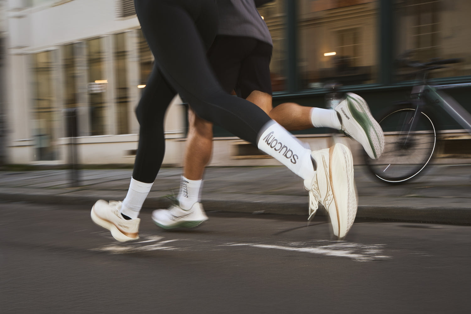 Zwei Läufer, nur die Beine sichtbar, laufen im Gleichschritt auf einer Straße durch die Stadt