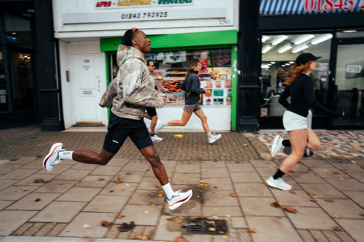 Eine Gruppe von Läufern in Saucony Ride 19 Laufschuhen joggt an einem Laden mit grüner Fassade vorbei.