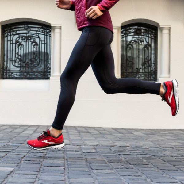 Sportler beim Training in Brooks-Lauftights und roten Brooks-Laufschuhen auf Kopfsteinpflaster. Fokus auf die Passform der schwarzen Running-Tight.